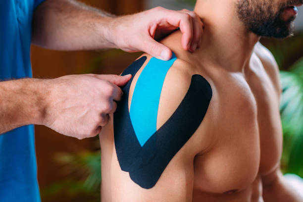 therapist taping man’s shoulder with elastic therapeutic kinesiology tape - kinesio imagens e fotografias de stock