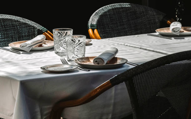 two glasses stand out on a restaurant table set for three on a white tablecloth - restaurant tablecloth imagens e fotografias de stock