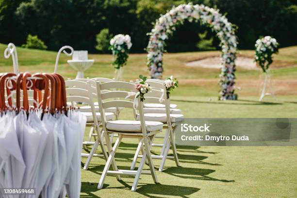 White Wooden Chairs With Rose Flowers On Each Side Of Archway Outdoors Copy Space Empty Chairs For Guests Prepared For Wedding Ceremony On Golf Course Stock Photo - Download Image Now
