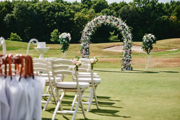 istock Place for wedding ceremony on green golf course, copy space. Wedding arch decorated with flowers and white chairs on each side of archway outdoors. Wedding setting 1308459469