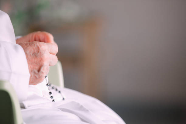 Detail of nun in deep prayer with rosary Nun dressed in white and sitting on the chair holding the rosary in hand and praying. Selective focus. Hope concept nun catholicism sister praying stock pictures, royalty-free photos & images