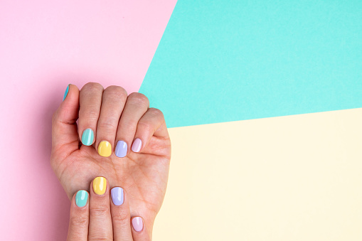 Hands with pastel nail polish on multicolored background.