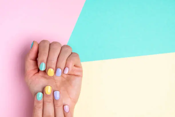 Bright trendy female manicure in funky spring colors. Woman's hands with pastel manicure on yellow, pink and blue background. Beautiful multi colour spring Easter manicure. A lot of space for text.