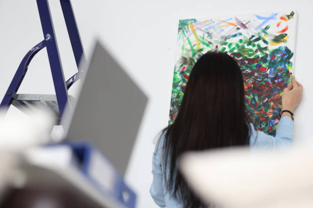 istock Brunette woman hangs her painted picture on wall 1308464058