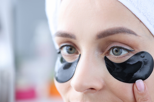 Woman uses black patches under eyes to eliminate swelling and smooth wrinkles. Morning facial procedures concept