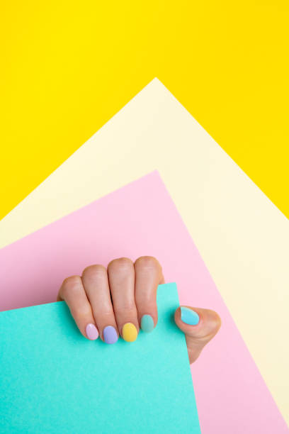 istock Hand with pastel nail polish, holding a paper on multicolored background. 1308467839