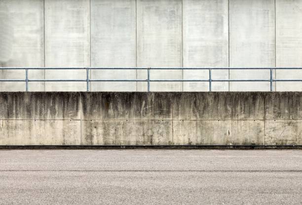 istock Railing on a grunge concrete wall dividing an asphalt road from a concrete building. 1308468366