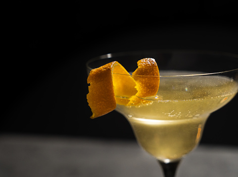 Front view of a Pornstar Martini cocktail with a shot of Prosecco  on a bar counter. The background of the image is defocused lights and the back of the bar. This cocktail has passionfruit as a garnish on the cold drink.
