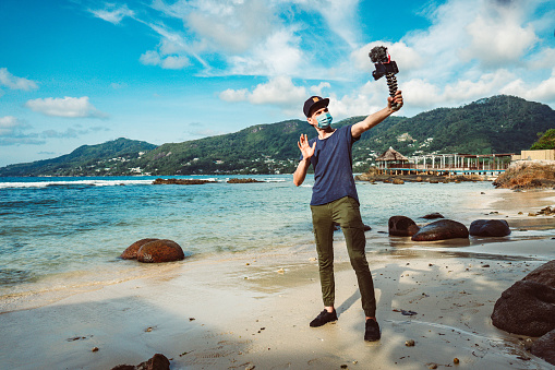 He films himself on video camera, Indian Ocean and coastline behind