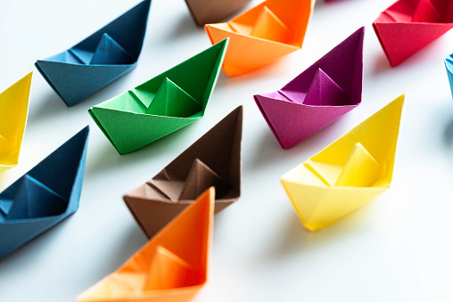 Multi coloured paper boats on white background.