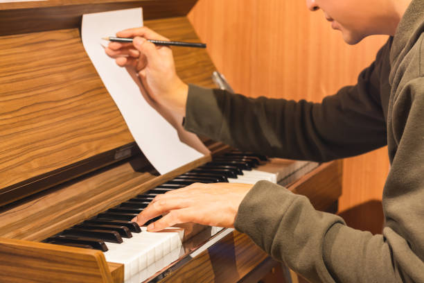 male composer playing piano and writing a song on music sheet