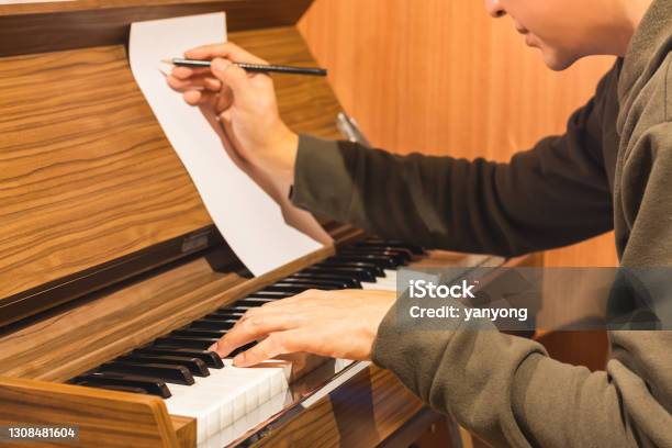 Male Composer Playing Piano And Writing A Song On Music Sheet Stock Photo - Download Image Now