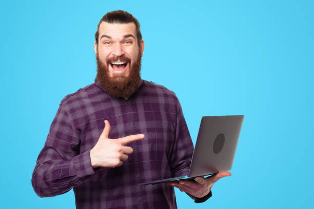 istock Amazed young bearded man pointing at laptop and smiling 1308484978