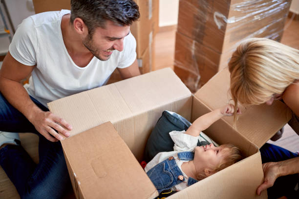 padres jugando con su hija escondido en caja de cartón.  nuevo apartamento, nuevo comienzo, alegría, juguetón, despreocupado, concepto de ocio - beginning of life fotografías e imágenes de stock