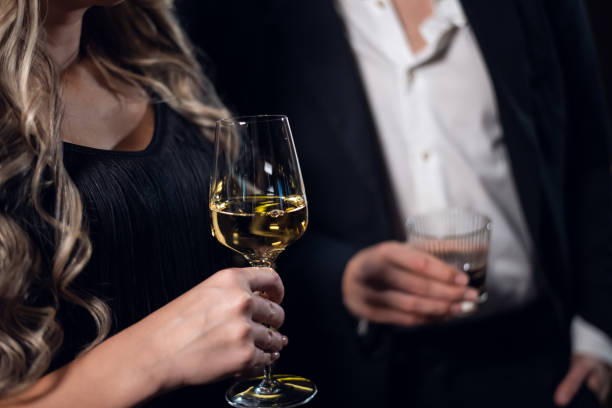 a blonde girl in a black dress holding a glass of champagne, a man in a jacket holding a glass of whiskey, close-up stock photo