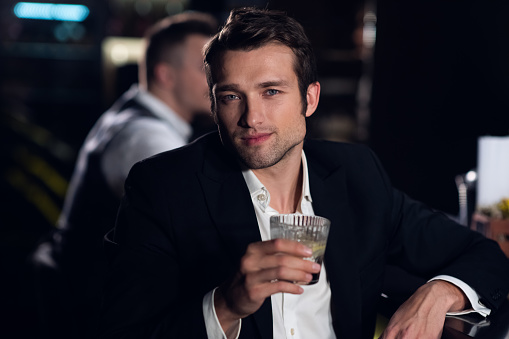 portrait of a young man in a shirt and jacket at the bar with a cocktail in his hands.