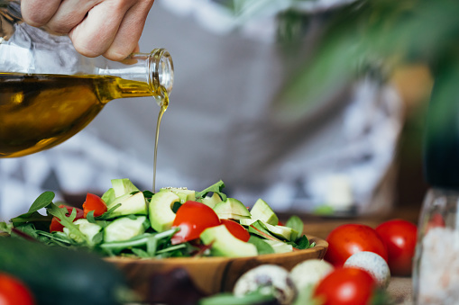 Hand pouring olive oil on the salad with tomatoes, avocado and cucumber.