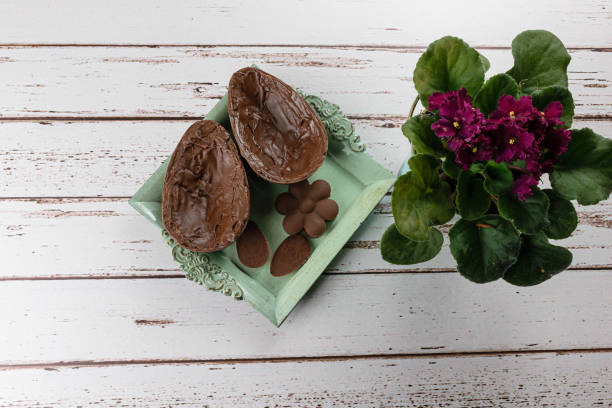istock Two halves of chocolate Easter egg, on a small old tray. Next to mini chocolates and flowers (top view). 1308493437