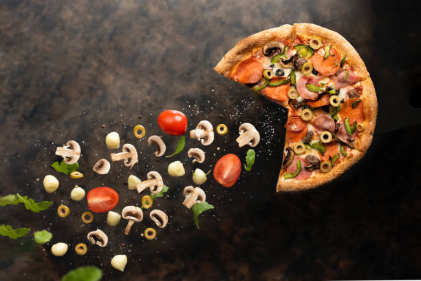 Flying hot pepperoni pizza with ingridients on slate background