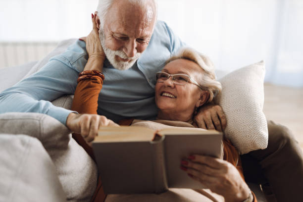 istock Happy mature couple in love talking while reading a book  at home 1308494839