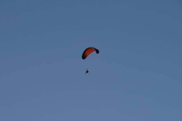 istock orange black paraglider with fan in blue sky - diagonal 1308501487
