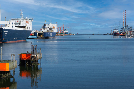 A view of Dublin Port, Ireland, with ships berthed on the left, the Poolbeg Towers on the right and the Poolbeg Lighthouse in the distance.