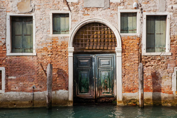 Venice, Italy - June 2nd 2024:  Closed wooden door and grated windows in a weathered brownstone wall