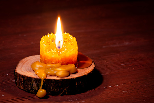 Burning beeswax candle on a tree stump. Close-up shot with copy space.