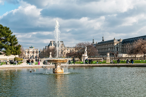 Paris : fountain in Jardin des Tuileries in spring, with Louvre museum in background. France, March 19, 2021.