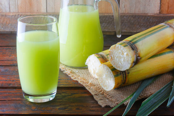 Fresh sugar cane juice in a jar with cut pieces of cane on rustic wooden restaurant table stock photo