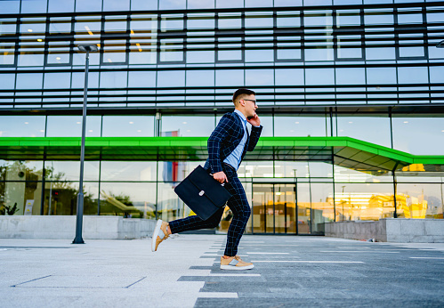 Happy young businessman in formalwear using smart phone while running to work