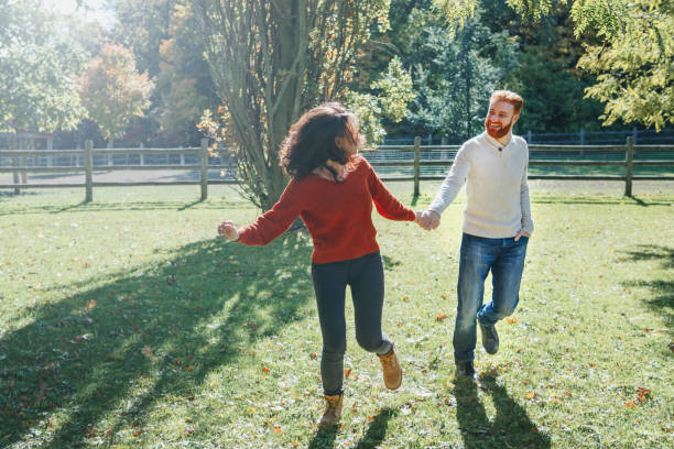 homme et femme heureux de couples dans l’amour marchant dans le stationnement extérieur. belles personnes hétérosexuelles caucasiennes belles datant marchant un jour d’été d’automne d’automne. personnes adultes retenant des mains. - women love heterosexual couple color image photos et images de collection