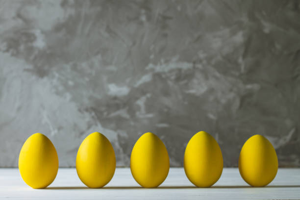 fila de cinco huevos de pascua amarillo brillante, de pie sobre la superficie de madera blanca sobre fondo de hormigón gris. copiar espacio - colores fotos fotografías e imágenes de stock