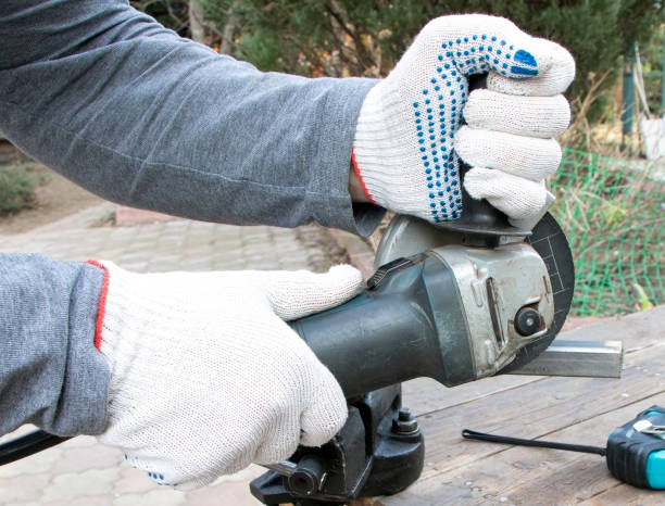 istock Men's hands holding a angular grinding machine. Woker is cutting a metal profile. Old vise on a wooden bakground. Old instrument. Angle grinder in hands. 1308522150