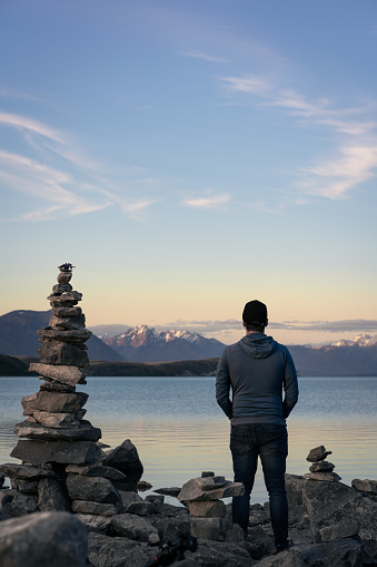 Man standing next to a tower of rock balancing in front of Lake Tekapo. New Zealand. Vertical photography