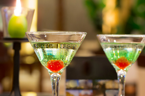 Two green apple martinis with cherry garnish in a bar or restaurant.