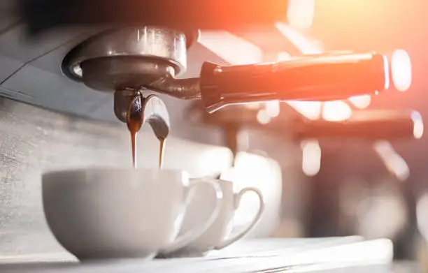 Low angle of coffee machine pouring fresh aromatic espresso in small mugs in cafe