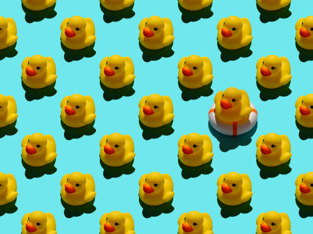 istock Many yellow rubber ducks in an abstract formal repeating pattern of following directional lines, with one yellow rubber duck sitting on an inflatable life belt standing out from the crowd, set on a turquoise background. 1308536849