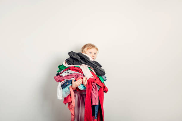 Mommy little helper. Cute Caucasian girl sorting clothes. Adorable funny child arranging organazing clothing. Kid holding messy stack pile of clothes, things. Home chores housework. stock photo