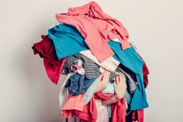 mamá pequeña ayudante. linda chica caucásica clasificando ropa. adorable niño divertido arreglando la ropa de organazing. chico sosteniendo un montón desordenado de ropa, cosas. tareas domésticas tareas domésticas. - washing fotografías e imágenes de stock