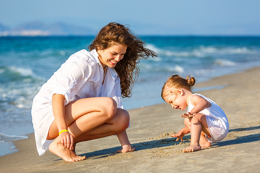 Mother and little daughter playing on the sea beach in Greece