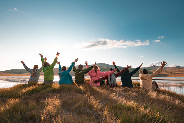 Big group of tourists sits with raised arms at sunset lake Big group of happy tourists are sitting with raised arms at beautiful sunset lake and mountains western siberia stock pictures, royalty-free photos & images