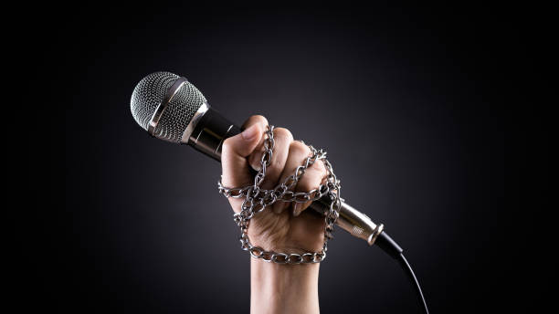 istock World press freedom day concept. Hand holding a microphone with chain on dark background, symbol of press freedom or speech freedom. 1308549931