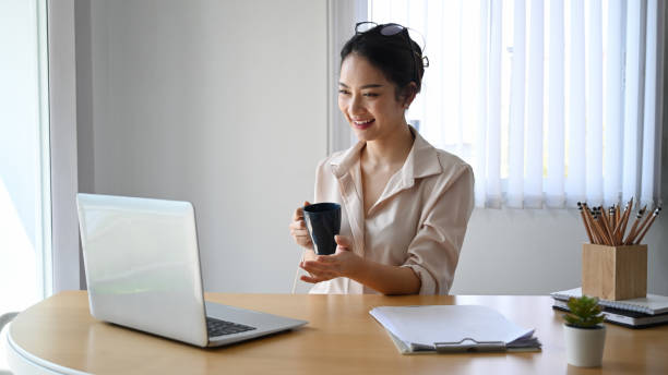 istock Cheerful businesswoman holding coffee cup and using laptop computer making video call with colleagues. 1308551646