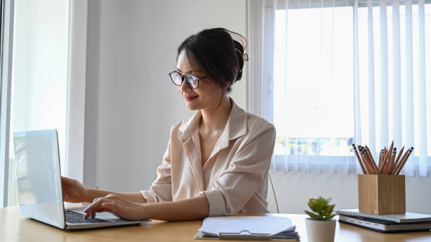 istock Smiling young woman office worker in eyeglasses working on laptop computer in office. 1308552262