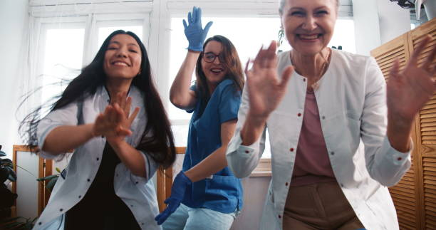 end of fighting coronavirus. zoom out three fun multiethnic happy female doctors dancing together at clinic lab office. - zoom victory imagens e fotografias de stock