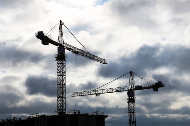 istock Silhouettes of construction cranes and workers against dark sky with storm clouds 1308558993