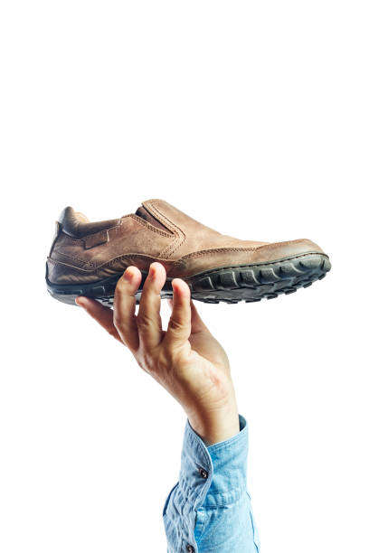 istock Hand of a man holding a brown shoe on a white background. Concept selection 1308560676