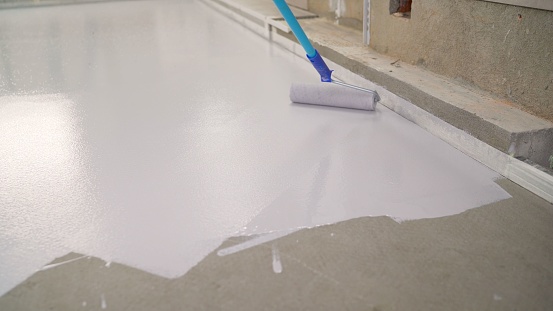 Pintura manual de un suelo blanco con rodillo de pintura para impermeabilización. Un trabajador pinta el suelo de hormigón con pintura blanca. Un trabajador pinta el suelo con un rodillo. photo