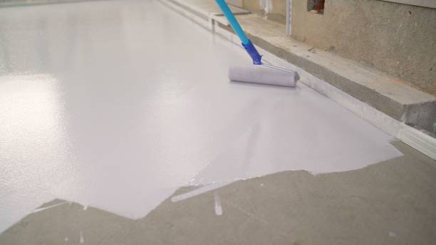 Manual painting of a white floor with a paint roller for waterproofing. A worker paints the concrete floor with white paint. A worker paints the floor with a roller. stock photo